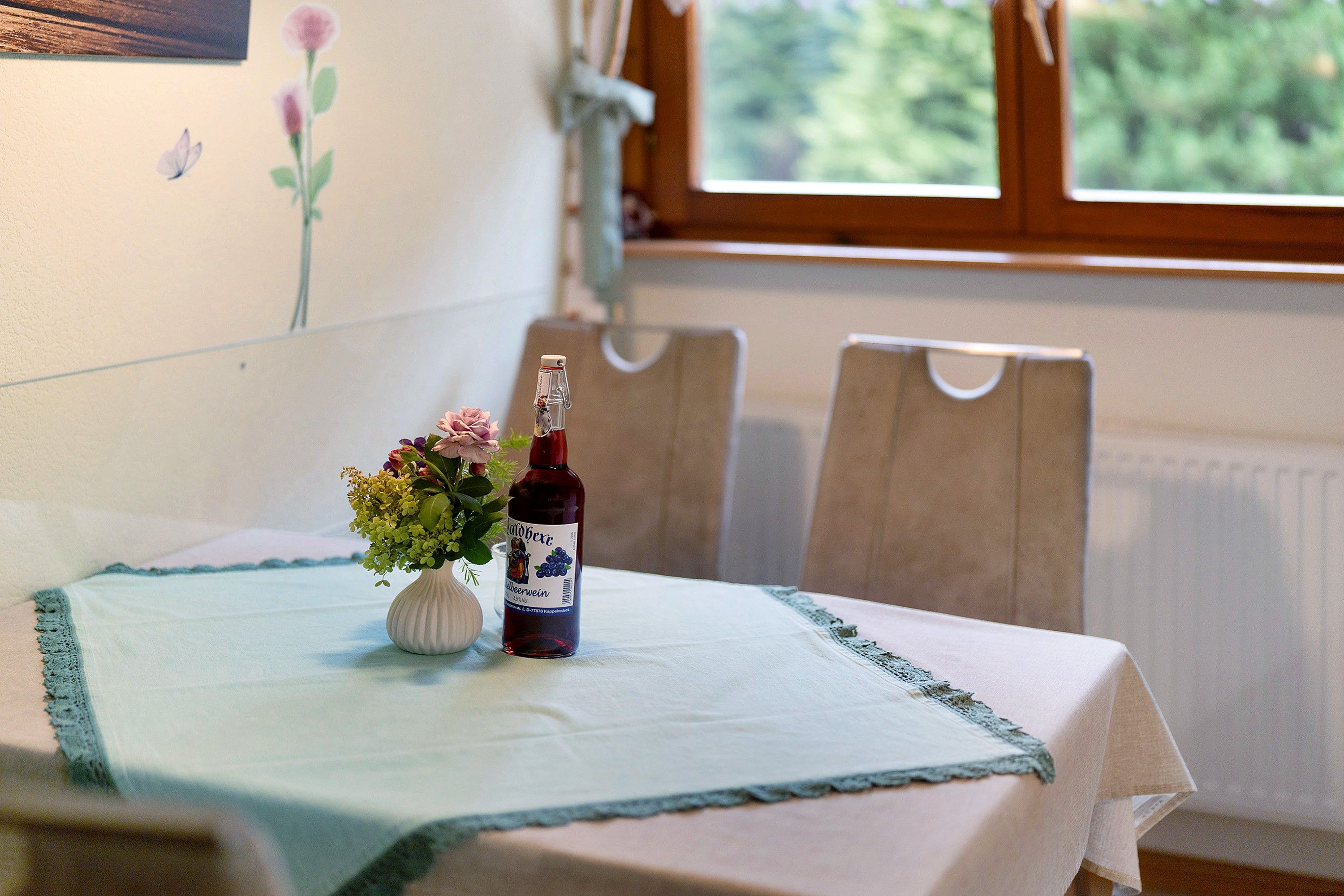 A table with a bottle of wine and a vase of flowers on a tablecloth.