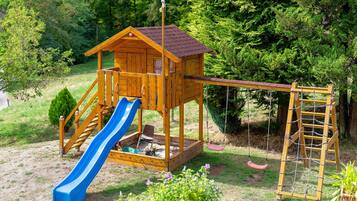 A wooden playhouse with a slide and a rope ladder.