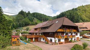Ein traditionelles Chalet mit geneigtem Dach, Holzbalkonen und einem Ziegelhof.