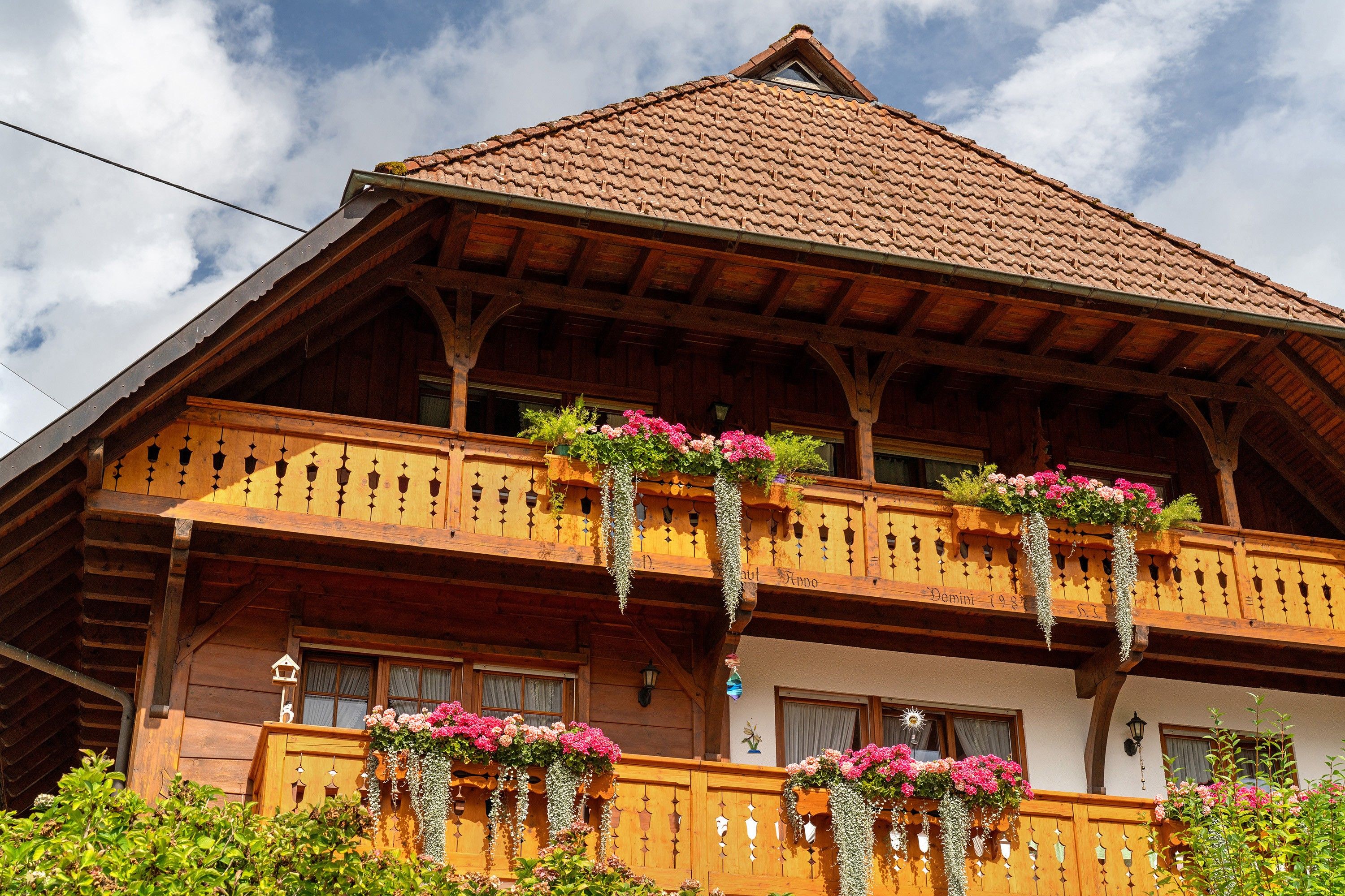 A traditional wooden chalet with a sloped roof and a balcony adorned with hanging flower baskets.