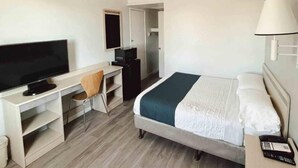 Quarto de hotel com cama, escrivaninha, cadeira, televisão e mesa de cabeceira com abajur.