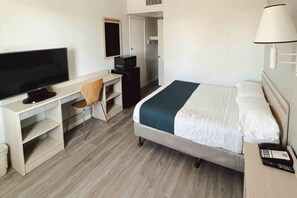 A hotel room with a bed, a desk with a chair, a television, and a bedside table with a lamp. - ADA Queen Bed|RI Shower|Smoking (Holbrook)