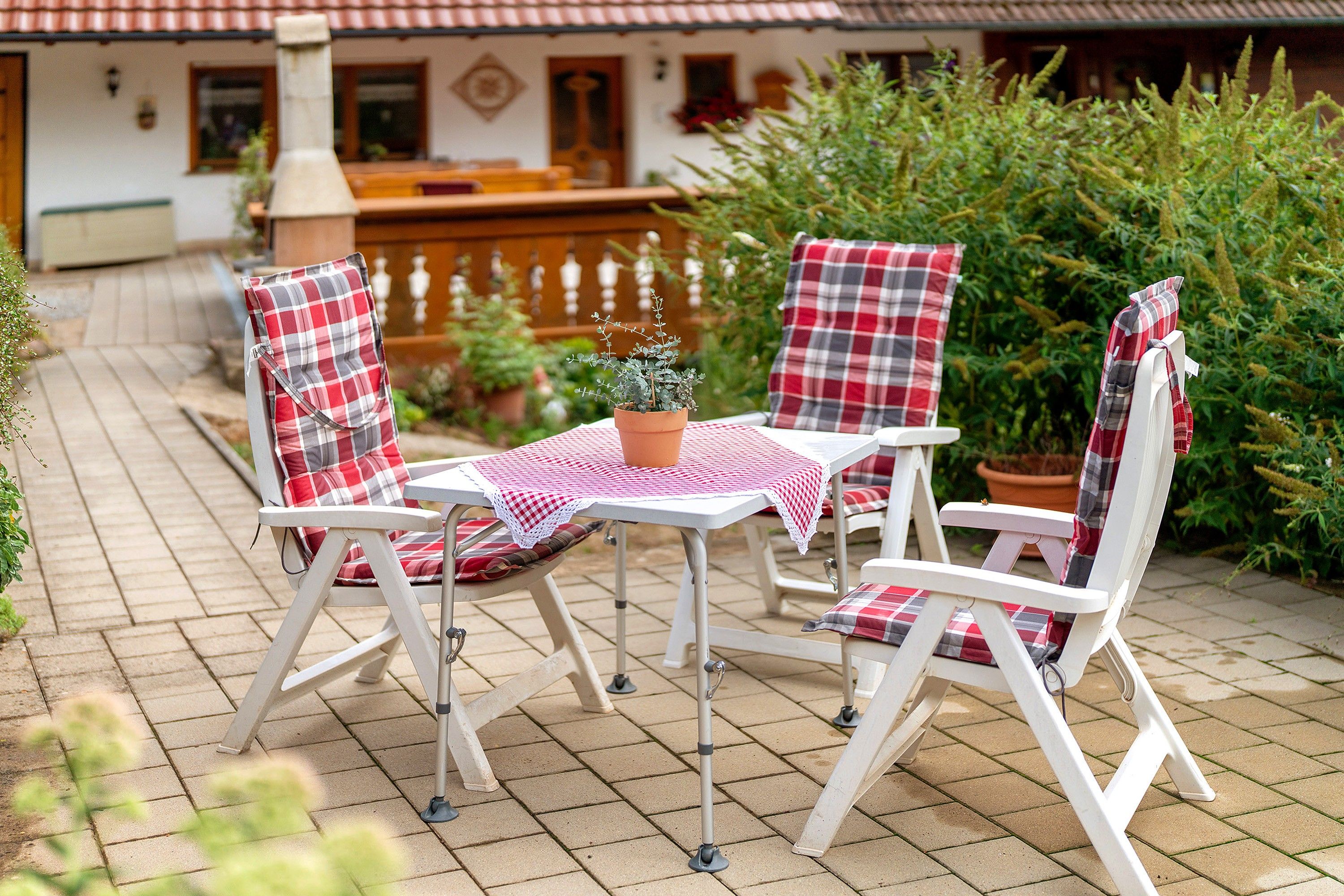 A patio with a table and four chairs, a potted plant, and a brick pathway.