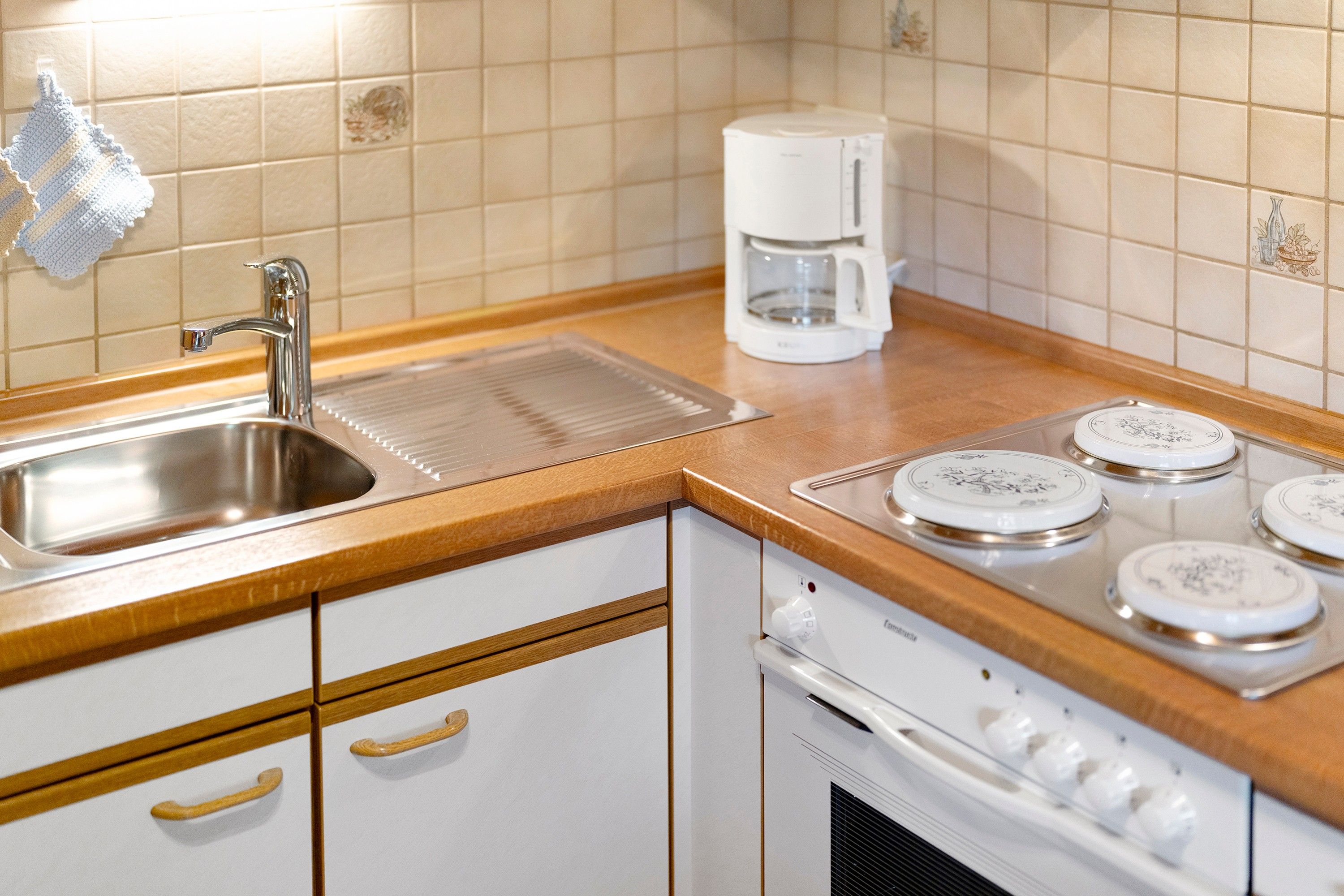 A kitchen with a stainless steel sink, a coffee maker, and a stove with four burners.