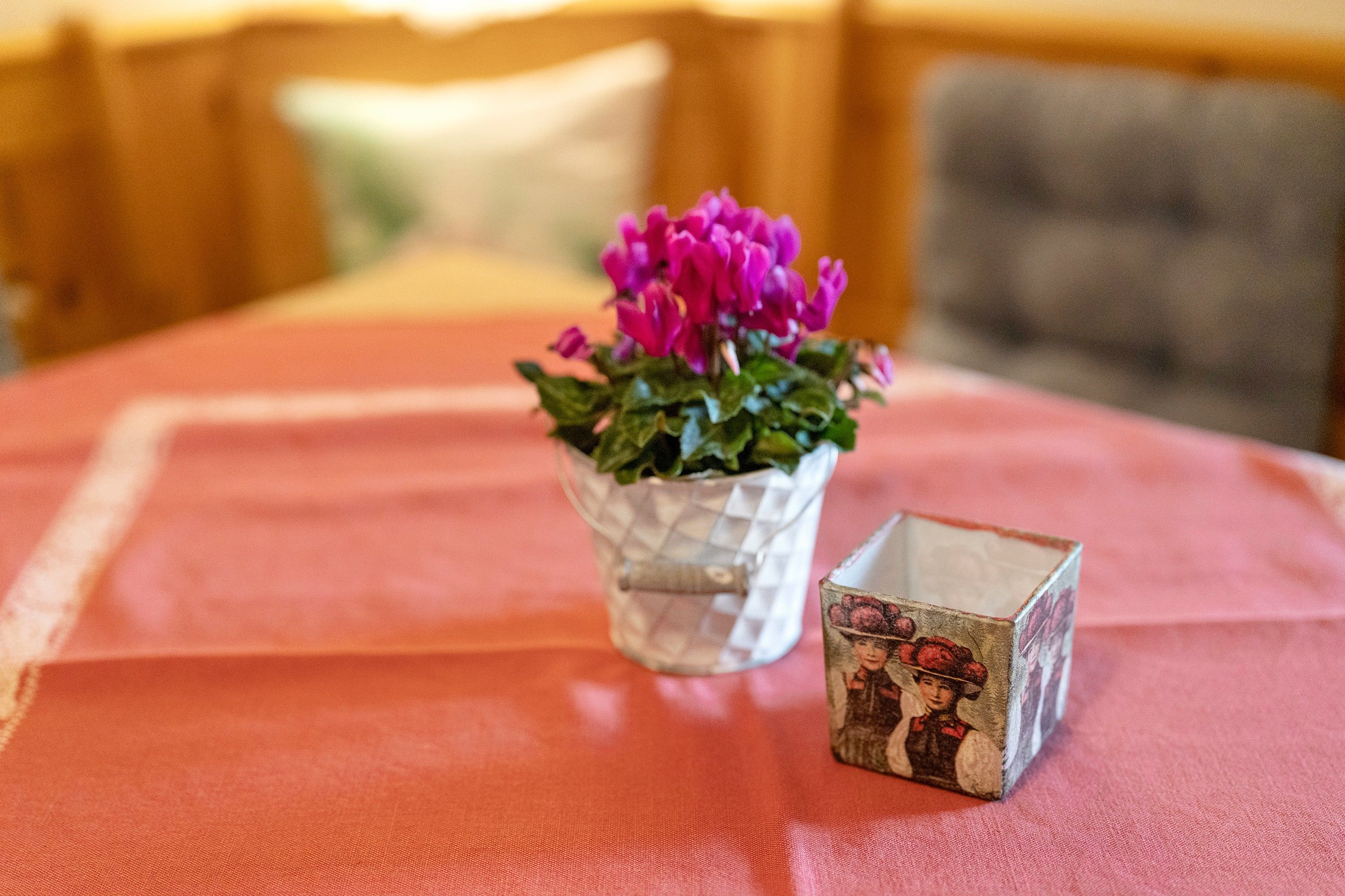 Ein Tisch mit roter Tischdecke, eine klare Glasvase mit rosa Blumen und eine kleine, dekorative Schachtel im Vintage-Stil.