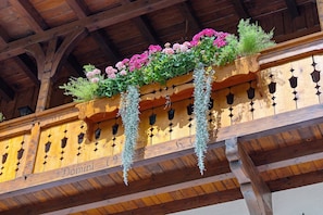 Un balcone in legno con ringhiera in ferro battuto, una targa in legno con il nome 'Domini' e cesti di fiori pensili con fiori rosa e verde.