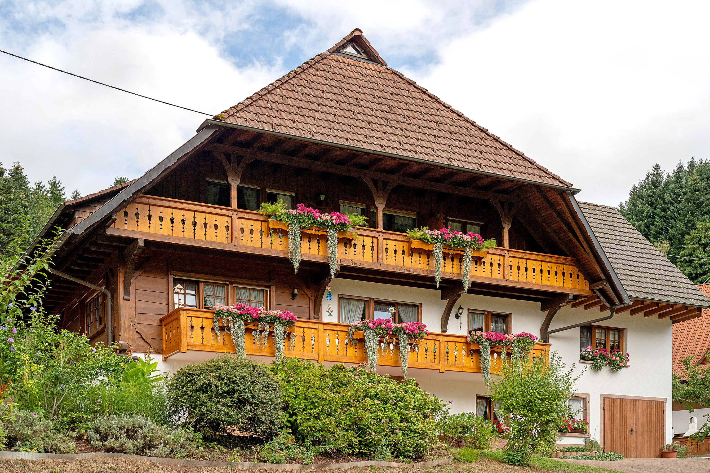 A traditional wooden chalet with a steeply pitched roof, wooden balconies with flower boxes, and a well-maintained garden.