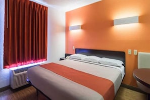 Quarto de hotel com cama, mesa de cabeceira, cadeira, aquecedor e janela com cortinas.