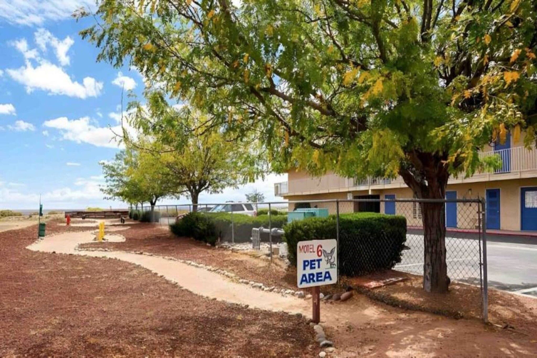 A motel with a sign indicating a pet area, surrounded by trees and a fenced parking lot.