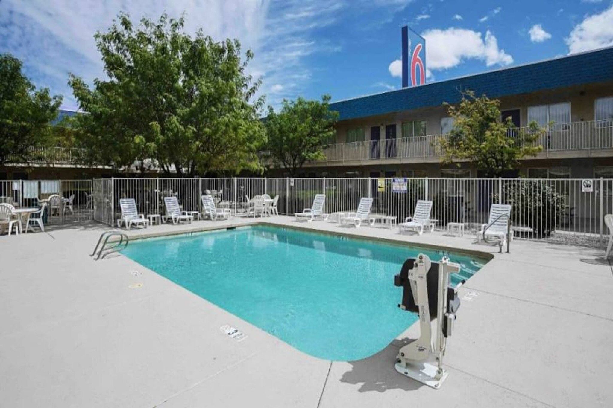 A swimming pool with lounge chairs, a lifeguard stand, and a building with a blue roof and a red logo in the background.