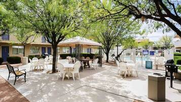 An outdoor patio area with tables and chairs, surrounded by trees and a building with a blue door.