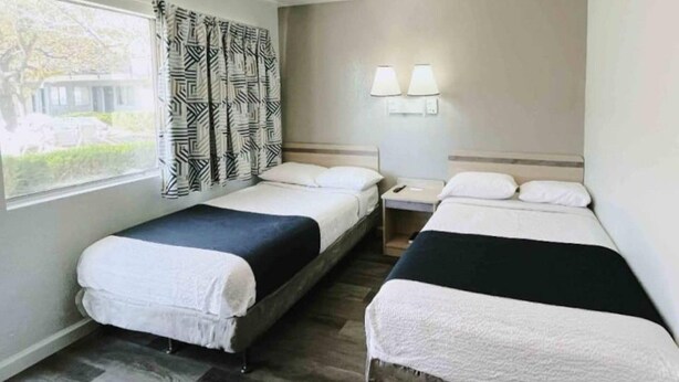 Ett hotellrum med två separata sängar, ett fönster med gardiner, ett nattduksbord med en lampa och utsikt över omgivningen.
