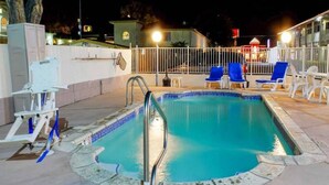 Ein Swimmingpool mit einer Metallleiter, umgeben von einem weißen Zaun und blauen Liegestühlen.
