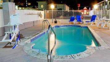 Ein Swimmingpool mit einer Metallleiter, umgeben von einem weißen Zaun und blauen Liegestühlen.