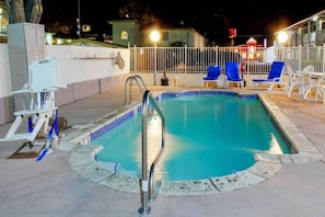 Una piscina con una escalera metálica, rodeada por una valla blanca y sillas reclinables azules.