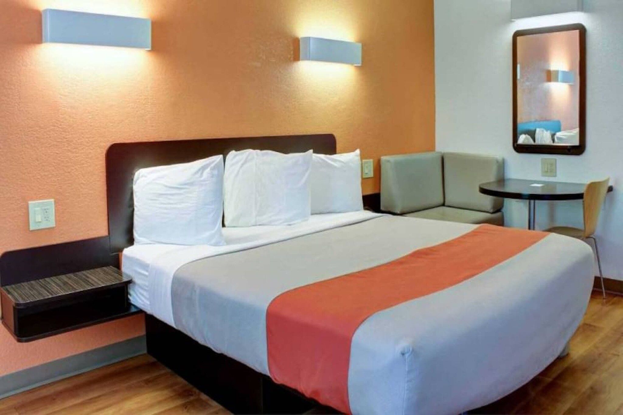 Ein Hotelzimmer mit Bett, Nachttischen, einem Sessel, einem kleinen Tisch und einem Spiegel an der Wand.