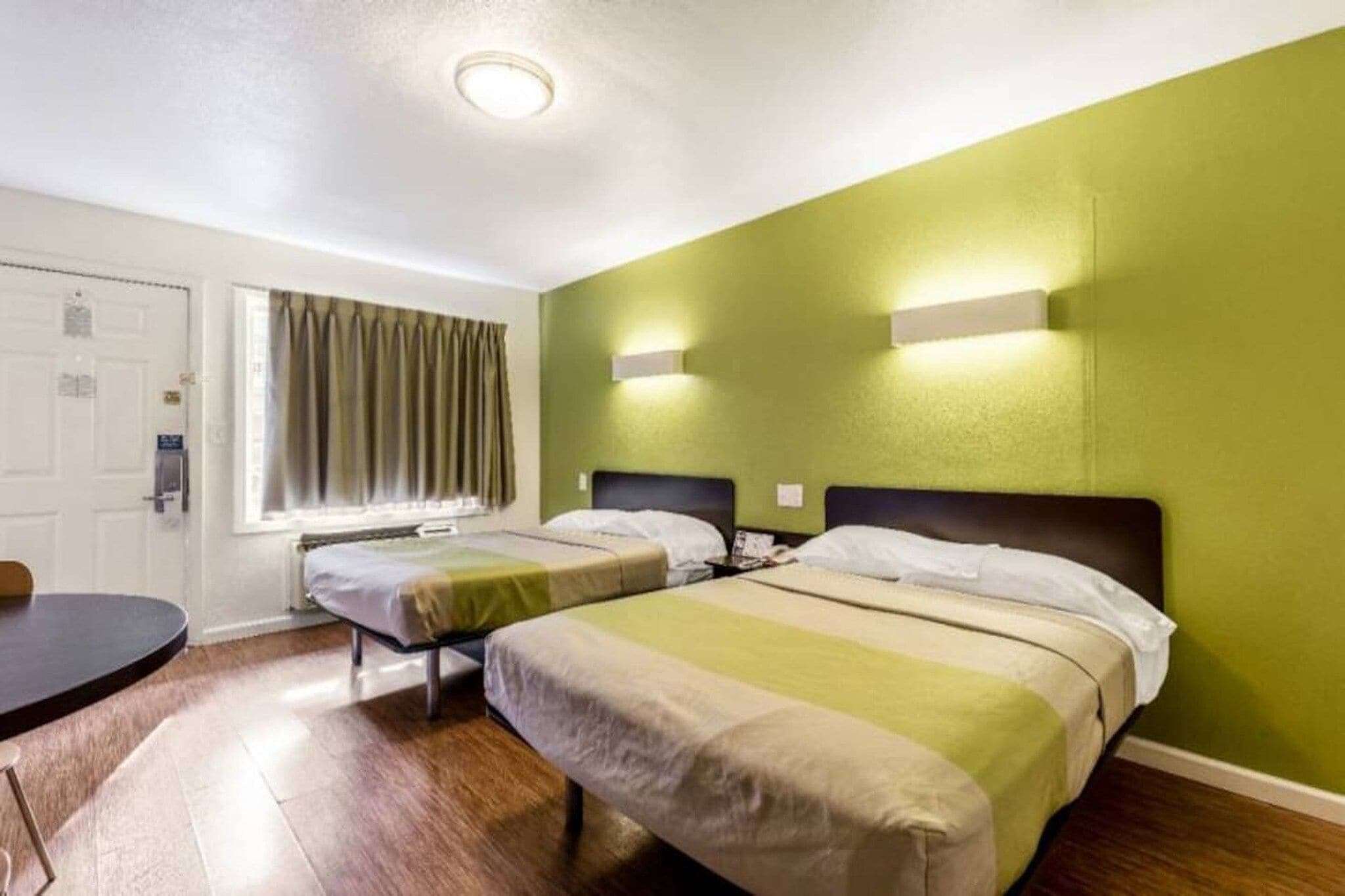A hotel room with two beds, a window with curtains, a desk, and a door.