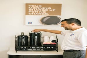A person in a white shirt pointing at a coffee station with kettles and cups labeled 'FRESHLY BREWED COFFEE.' - 2 Full Beds|Accessible|Tub|Nsmk (San Rafael)
