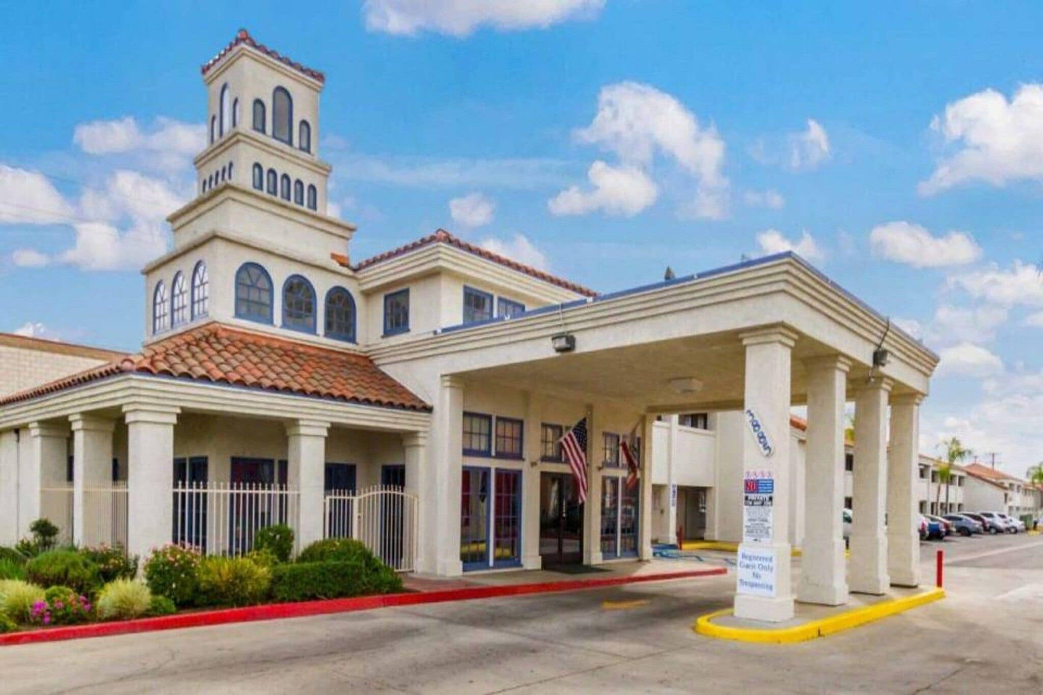 Un hotel con una torre central, un acceso cubierto y un estacionamiento.