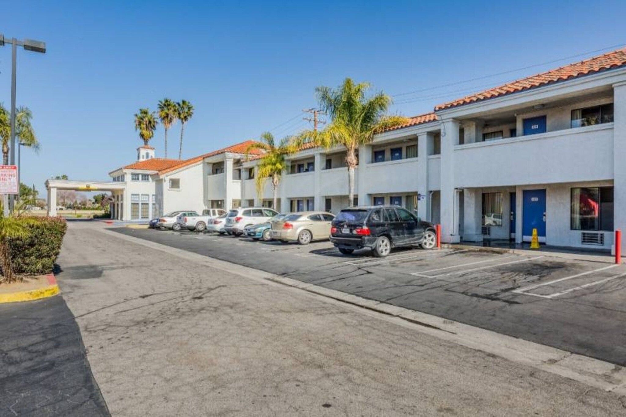 Une vue de rue d’une rangée de bâtiments d’un motel à deux étages, avec des voitures garées devant.