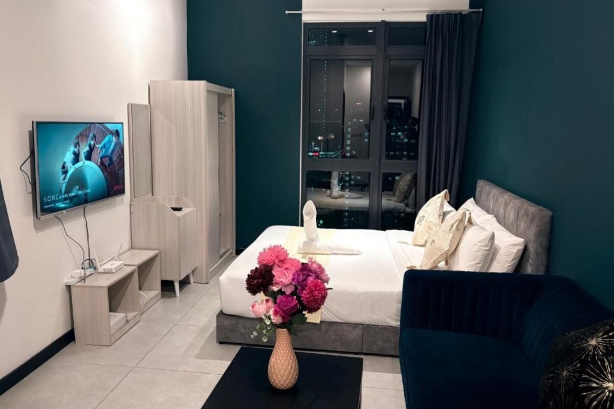 A modern hotel room with a bed, a TV, a desk, and a view of the city at night.