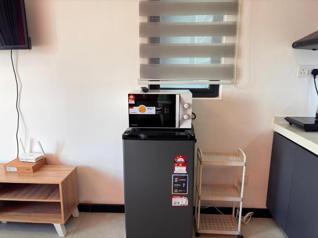 A compact kitchen with a microwave, a refrigerator, and a small wooden table with a box on it.