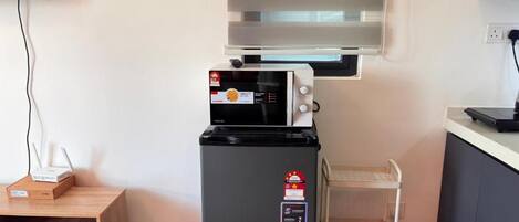 A compact kitchen with a microwave, a refrigerator, and a small wooden table with a box on it.