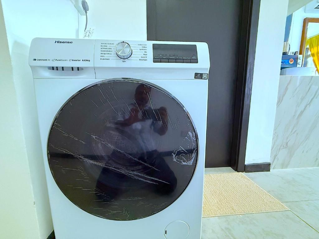 A white Hisense washing machine with a control panel, located in a room with a tiled floor and a door in the background.