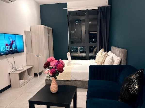 A modern hotel room with a bed, a TV, a desk, and a vase of flowers.