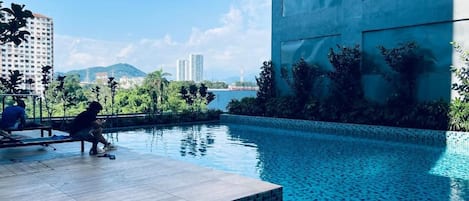 A swimming pool area with a view of a cityscape, including high-rise buildings and mountains in the distance.