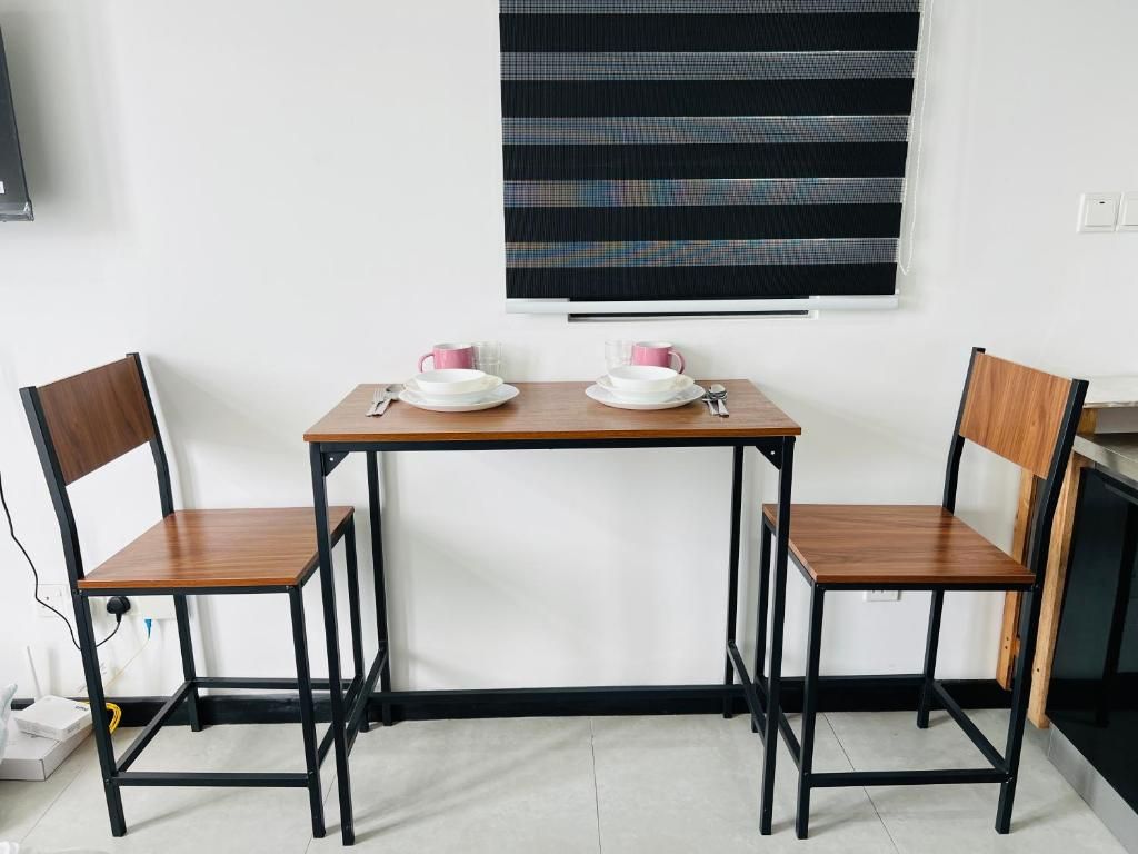 A small dining area with a table and two chairs, a window with a patterned blind, and a white wall.
