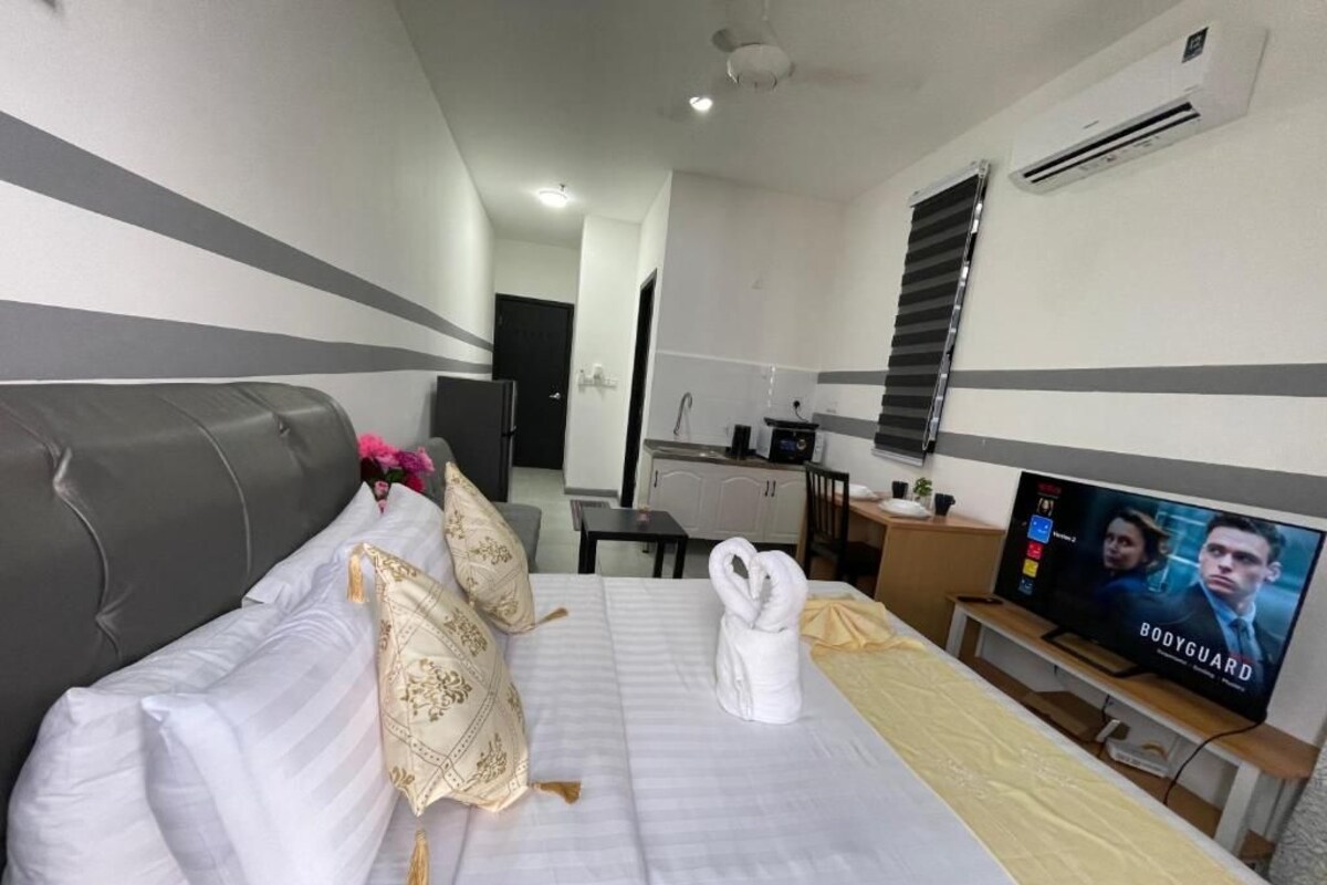 A hotel room with a bed, a television, a desk, and a kitchenette.