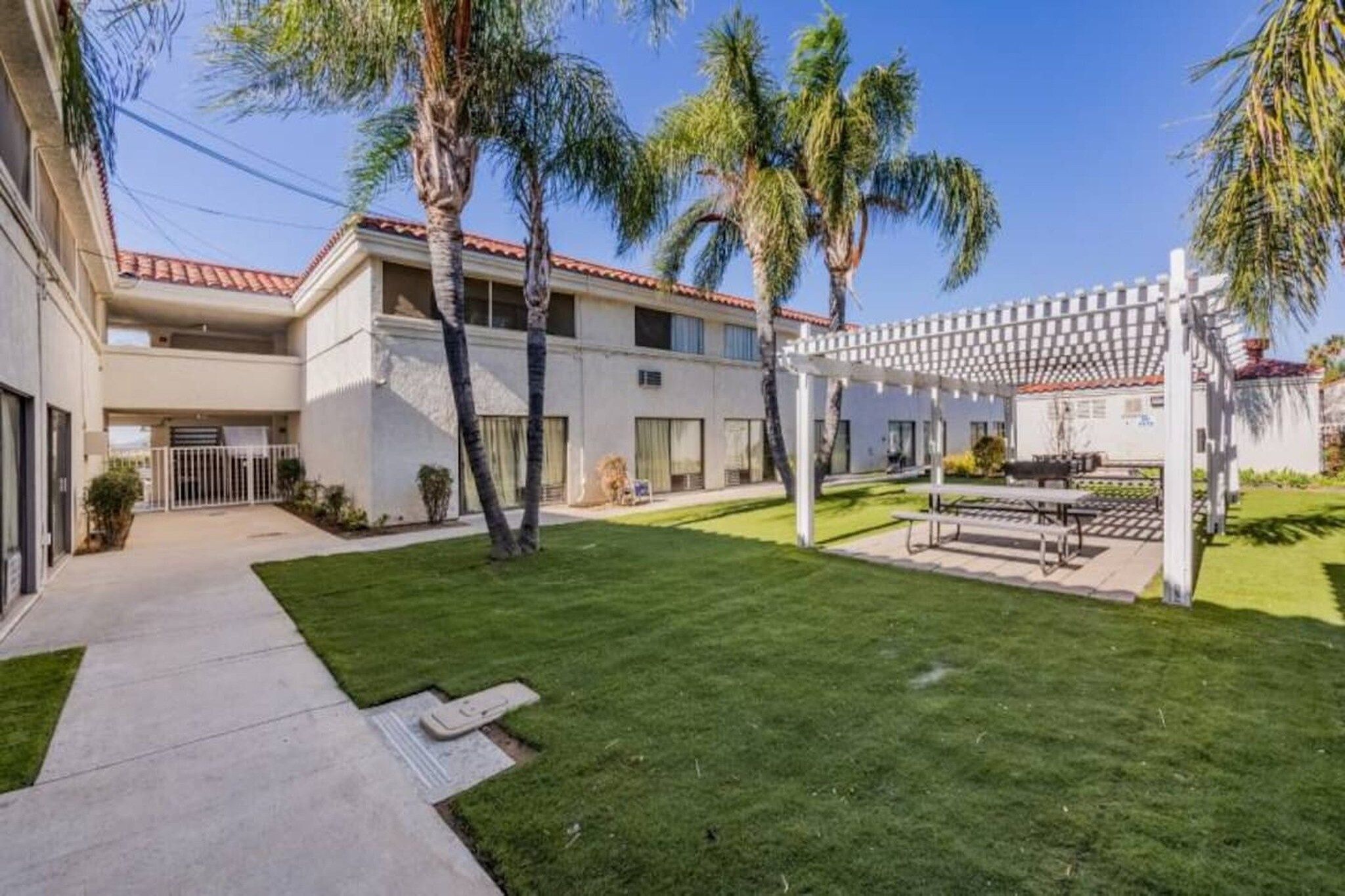 Un edificio residencial con un patio cubierto, palmeras y un césped bien cuidado.