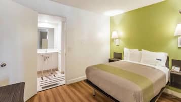 A hotel room with a bed, a nightstand, a lamp, a bathroom with a mirror, and a door.