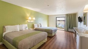 A hotel room with two beds, a desk, a chair, a window with curtains, and a flat-screen TV. - 2 Queen Beds|NS| Balcony (HEMET)