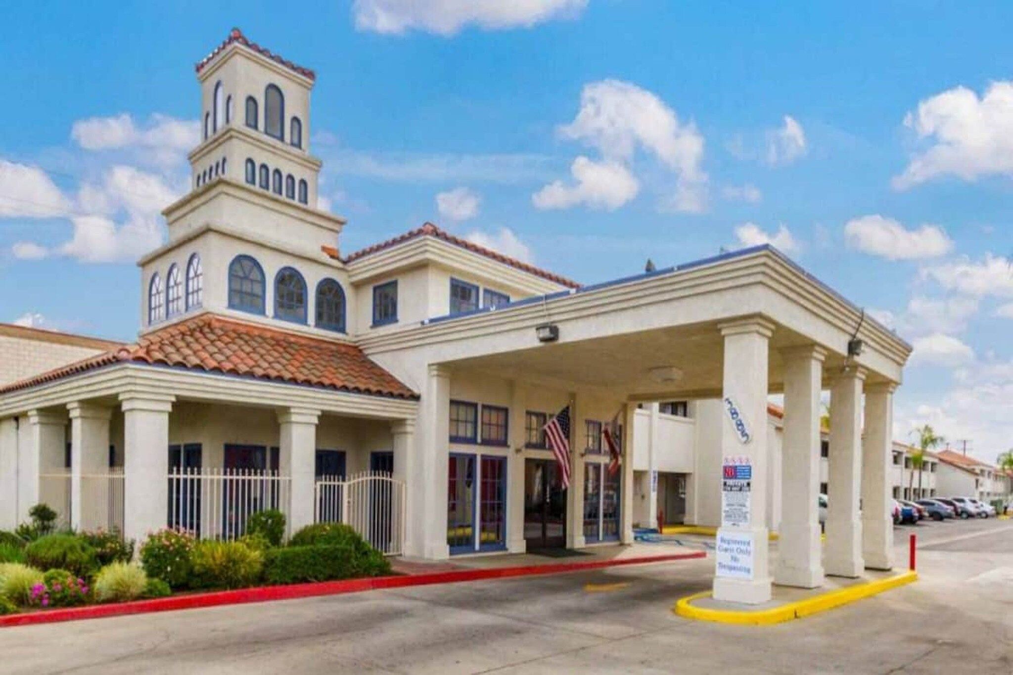 Un hotel con una torre central, una entrada cubierta y un estacionamiento.