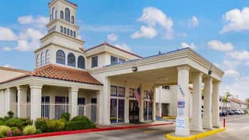 Un hotel con una torre central, una entrada cubierta y un estacionamiento.