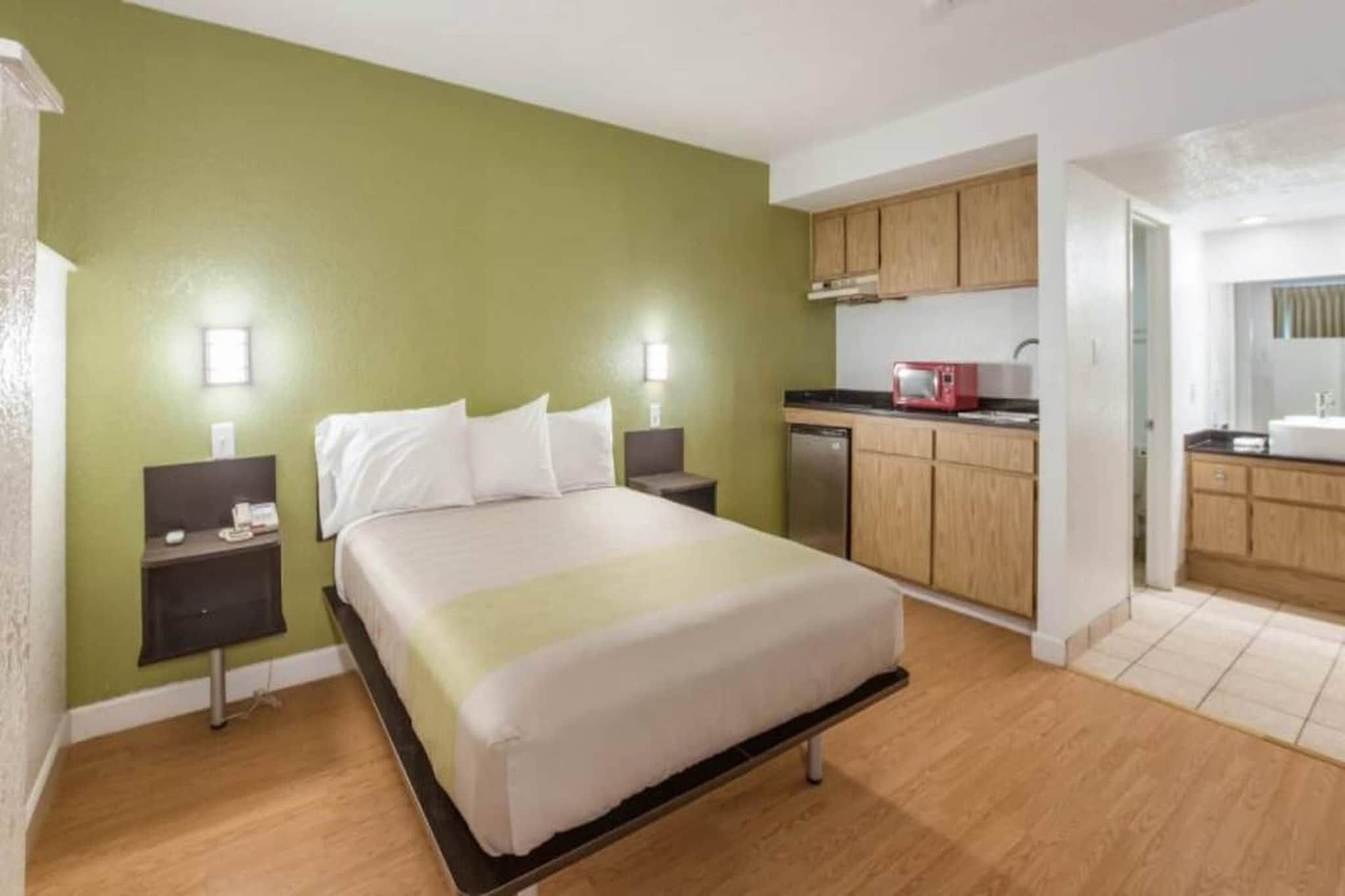 Quarto de hotel com cama, mesas de cabeceira, cozinha compacta e banheiro.