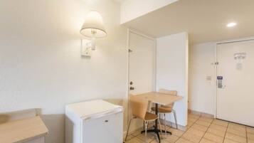 Una kitchenette pequeña con un refrigerador, una mesa con dos sillas y una lámpara de pared.