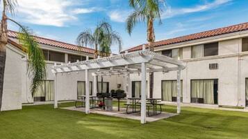 A courtyard with a covered seating area, palm trees, and a building with a tiled roof.