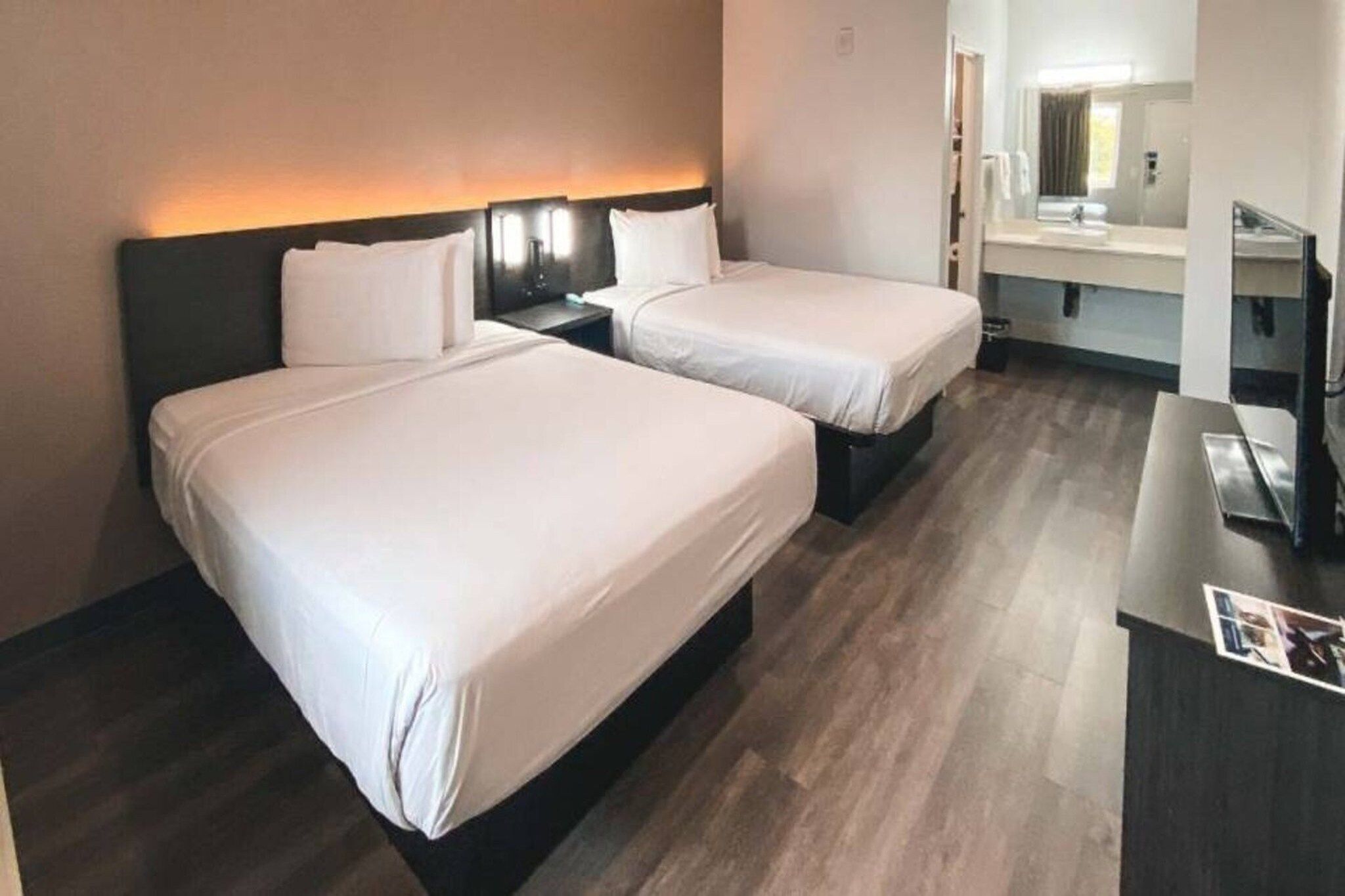 A hotel room with two beds, a desk, and a bathroom visible through an open door.