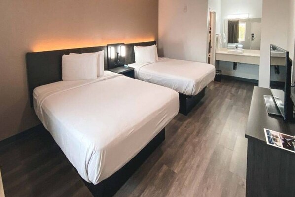 A hotel room with two beds, a desk, and a bathroom visible through an open door.