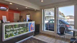 A hotel reception area with a large sign, a reception desk, a window view of parked cars, and a tiled floor. - 2 Queen Beds|NS| Kitchen (West Sacramento)