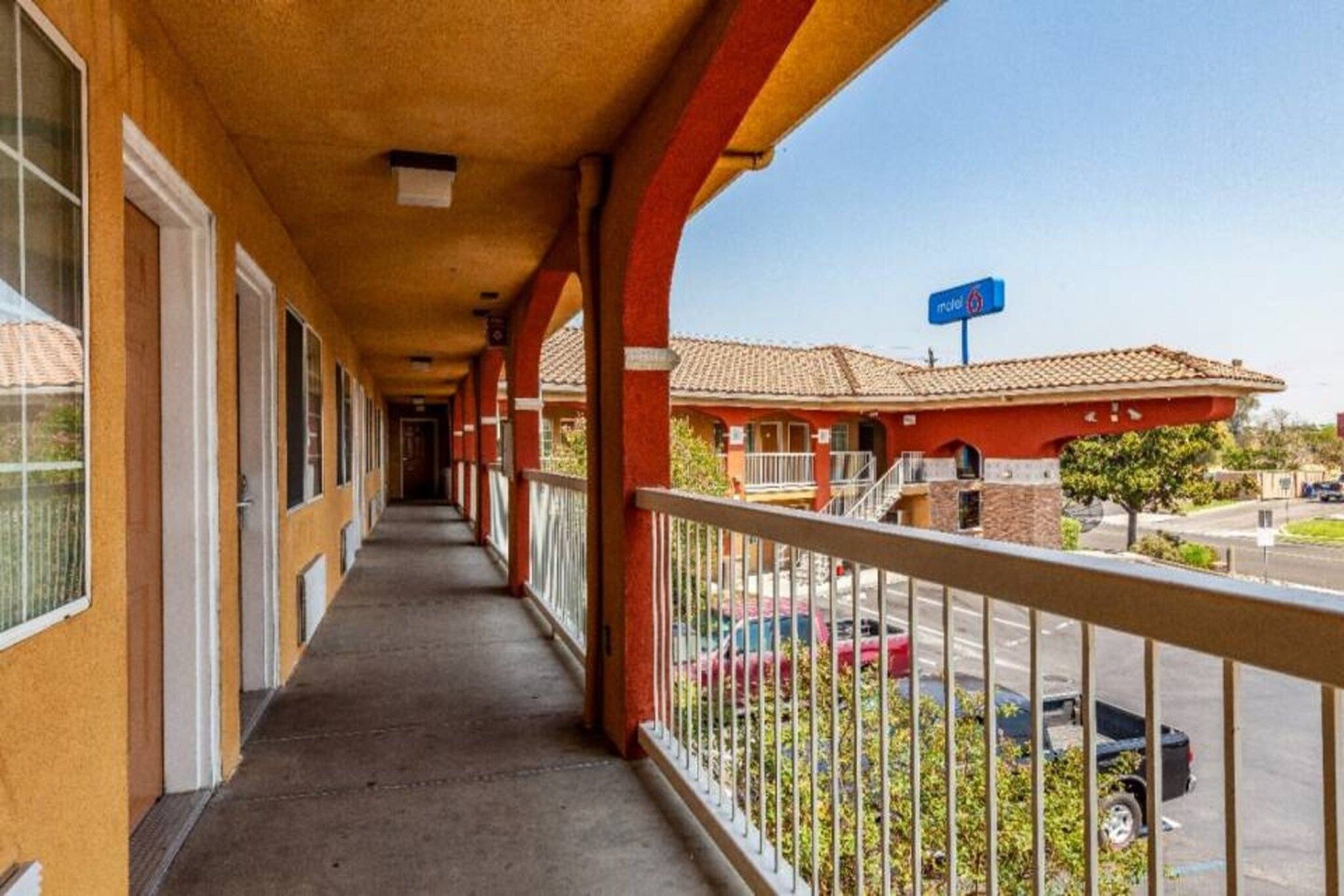 Ein Motelkorridor mit überdachtem Gang, ein rotes Gebäude mit einem Schild und ein Parkplatz mit Autos.