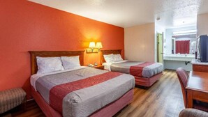 Ein Hotelzimmer mit zwei Betten, Holzboden, Schreibtisch und einem fensterbepflanzten Fenster.