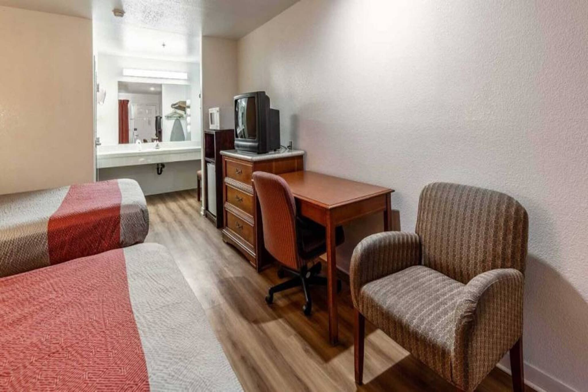 Ein Zimmer mit zwei Einzelbetten, einem Holztisch mit Stuhl, einem Fernseher und einem Spiegel.