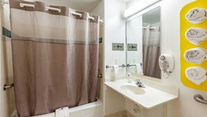 Ein Badezimmer mit Duschvorhang, Waschbecken, Spiegel und Handtuchhalter mit Handtüchern.