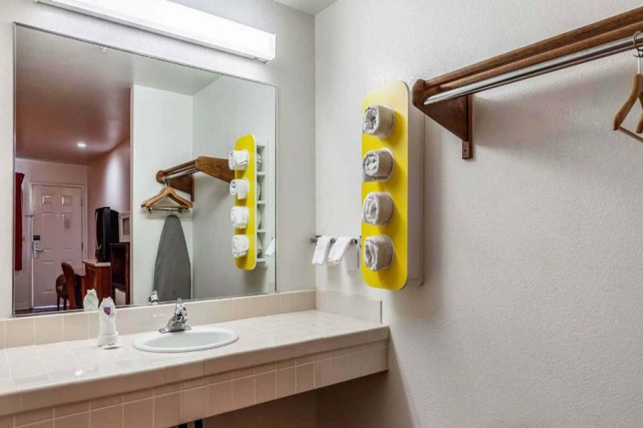 A bathroom with a sink, mirror, towel rack, and a towel dispenser.