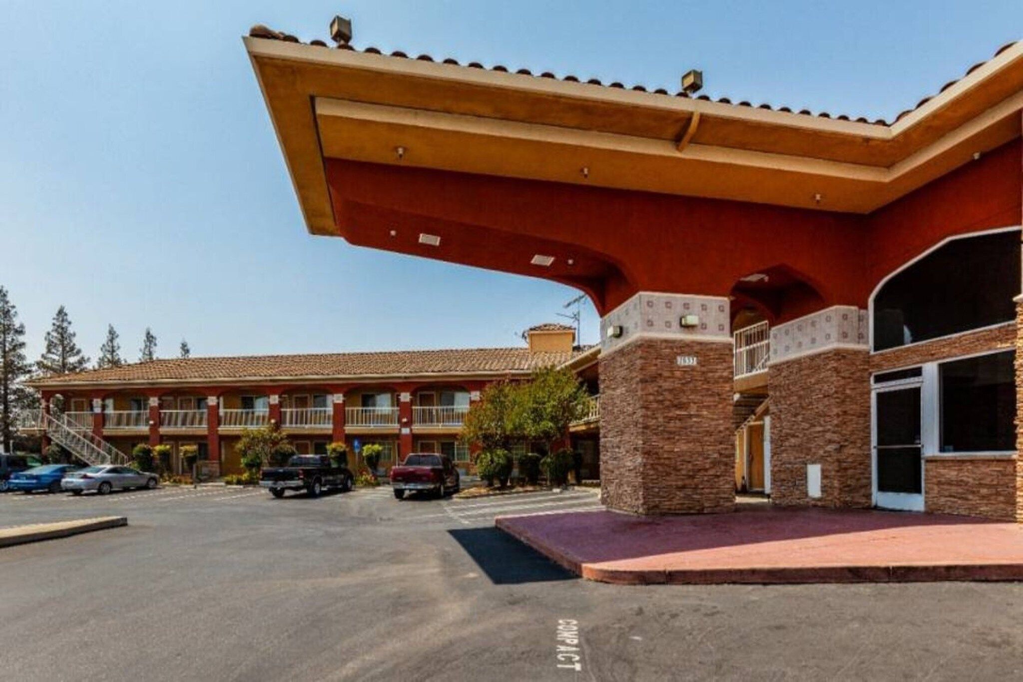 A hotel with a red facade, multiple balconies, and a parking lot with cars.