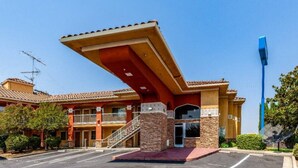 Hotel com fachada vermelha e amarela, entrada coberta e estacionamento.